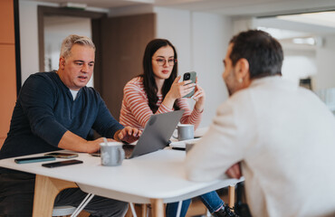 A multi-ethnic group of coworkers engaged in a casual business meeting with laptops and smart phones in a bright office.