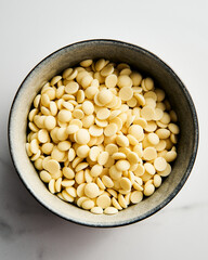 White chocolate drops in the bowl on white marble background. Baking ingredient