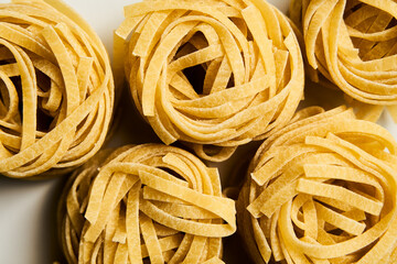 Dry tagliolini or tagliatelle pasta in nests in the bowl on white marble background. Uncooked ingredient