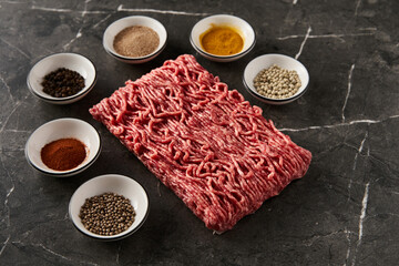 Raw and Fresh Minced Beef with spices for cooking on dark marble background. Minimalistic food photo, low-key.