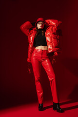Fashionable confident woman wearing trendy oversized red puffer down jacket, sunglasses, bucket...