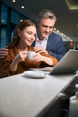 Adult caucasian man and woman with cup of tea or coffee watching laptop