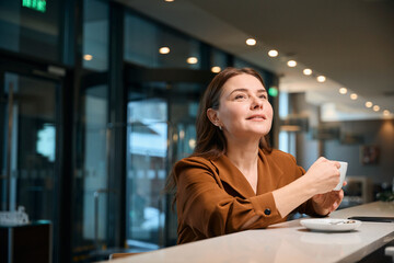 Adult thoughtful caucasian woman while drinking tea or coffee at reception desk