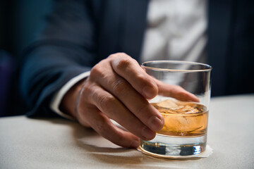 Close up of glass cup with cognac or whiskey in hands of blurred businessman