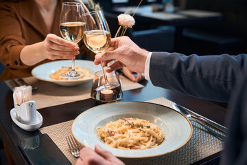 Cropped image of couple toasting wine from glasses in hotel restaurant
