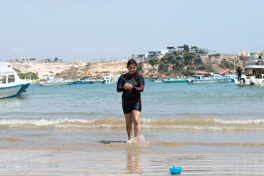 Ni&ntilde;a latina jugando con la arena en la playa al medio d&iacute;a con traje de ba&ntilde;o negro de mangas largas 