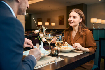 Happy woman and man eating pasta and looking at each other in hotel restaurant