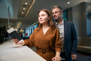 Adult couple with suitcases at reception desk during check-in in hotel lobby