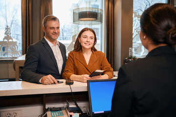 European couple looking at female reception desk during check-in in hotel lobby