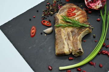 Grilled pork ribs with rosemary, chili pepper, garlic, and pomegranate on black stone background....
