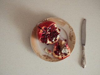 Horizontal straight from above close up of an open vibrant red pomegranate on a beige plate and a...