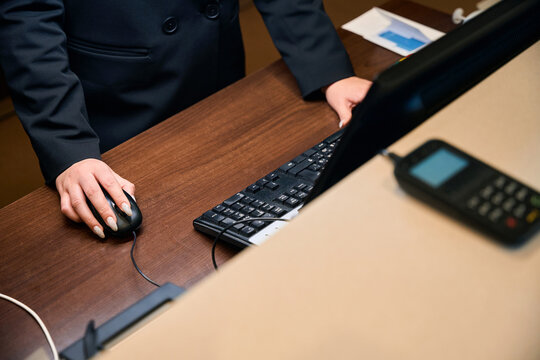 Partial of female receptionist using computer at reception desk in hotel lobby