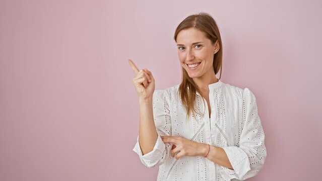 Young woman standing smiling happy pointing with hand and finger to the side over isolated pink background