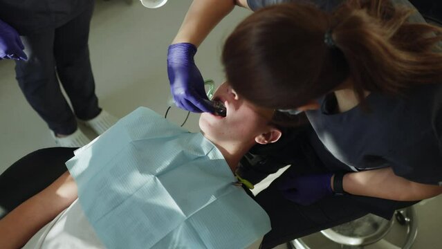 Close up woman dentist with assistant in medical masks hold dental instrument that treats teeth. Hydience and healthy