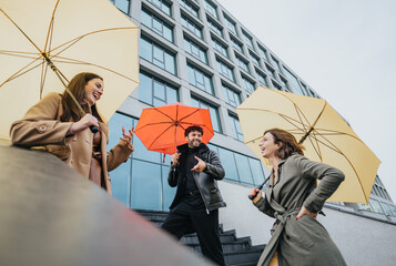 Three friends sharing a laugh during an urban walk, armed with colorful umbrellas on a cloudy day, embodying joy and friendship. © qunica.com