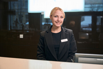 Female receptionist wearing uniform looking at camera at reception desk in hotel