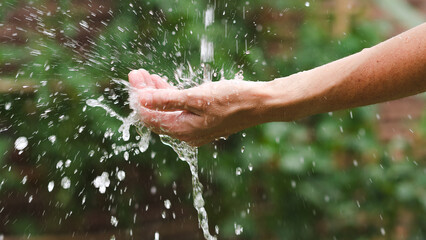 Woman's hand splashing water in the garden. Close up.