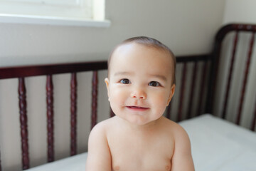baby in a crib smiling no shirt with a diaper