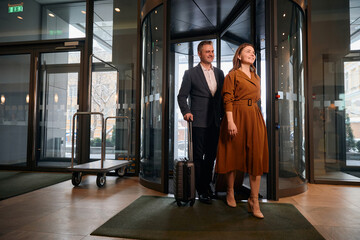 Adult caucasian couple with suitcases entering to hotel lobby at sunny day