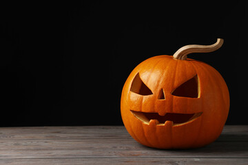 Scary jack o'lantern made of pumpkin on wooden table against black background, space for text....