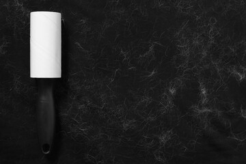 Lint roller and pet hair on black fabric, top view. Space for text