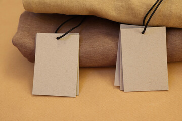 Garment with cardboard tags on kraft paper sheet, closeup. Space for text