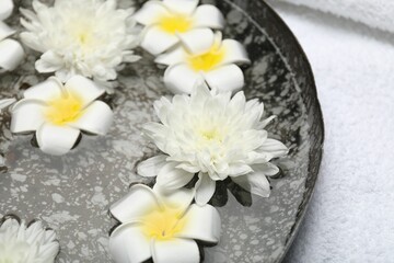 Bowl of water with flowers and towel on table, closeup. Spa treatment