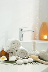 Spa composition. Rolled towels, herbal bags, cosmetic products and burning candles on white countertop in bathroom