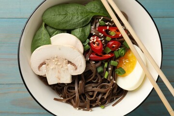 Tasty buckwheat noodles (soba) with chili pepper, egg, mushrooms and chopsticks on light blue wooden table, top view