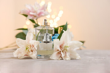 Fototapeta na wymiar Bottles of perfume and beautiful lily flowers on table against beige background with blurred lights, closeup. Space for text
