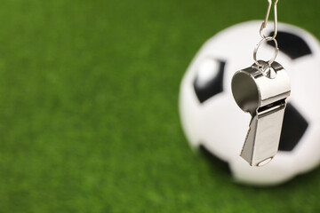 Football referee equipment. Metal whistle and soccer ball on green grass, closeup with space for...
