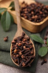 Wooden spoon with aromatic cloves and green leaves on table, closeup