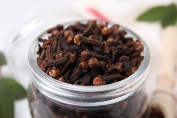 Aromatic cloves in glass jar on table, closeup