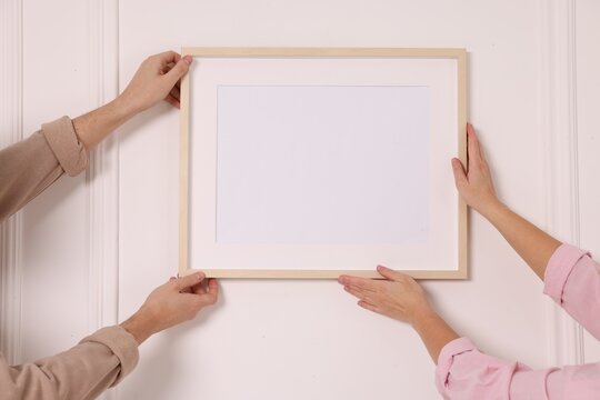 Man and woman hanging picture frame on white wall, closeup
