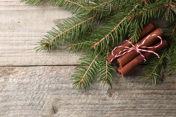 Cinnamon sticks and fir branches on wooden table, flat lay. Space for text