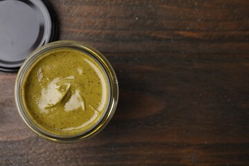 Tasty pistachio cream in jar on wooden table, top view. Space for text