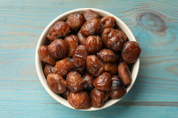 Roasted edible sweet chestnuts in bowl on light blue wooden table, top view
