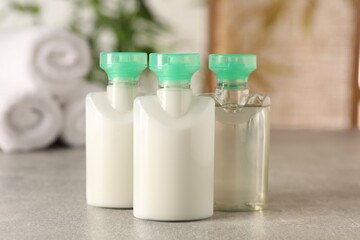 Mini bottles of cosmetic products on light grey table against blurred background, closeup