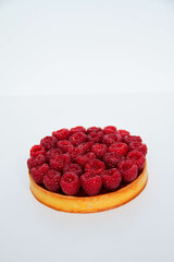 French dessert. Tart with raspberries with almond frangipane and raspberry coulis inside. Decorated with fresh raspberries. White background. Back view.