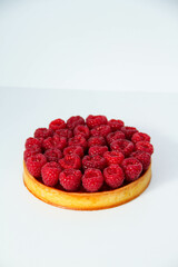 French dessert. Tart with raspberries with almond frangipane and raspberry coulis inside. Decorated with fresh raspberries. White background. Back view.