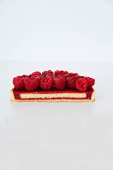 French dessert. Tart with raspberries with almond frangipane and raspberry coulis inside. Decorated with fresh raspberries. White background. Back view. The photo of textures inside of a tart.
