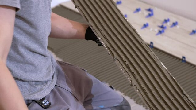 A tiler lays floor tiles on the floor. Porcelain tiles in the kitchen. A tiler is gluing tiles to the kitchen floor. A man is laying tiles on the bathroom floor.