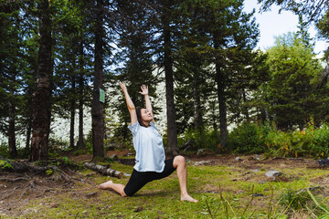 Yoga in nature in the forest, cute young girl exercising outdoors, leg stretching exercise, body bend back, balance asana.