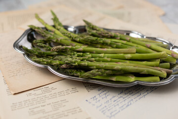 Close Up of Fresh Raw Asparagus on a Silver Plate with Old Recipes as Background