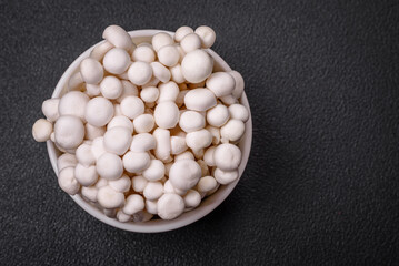 Small white edible beech mushrooms with salt and spices on a plain background