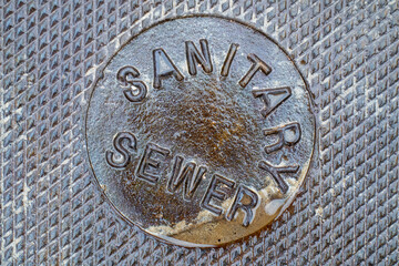 Close-up of old wet sandy Sanitary Sewer Manhole Cover