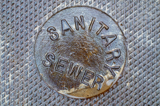 Close-up of old wet sandy Sanitary Sewer Manhole Cover
