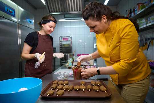 Team of confectioners making batch of cakesicles on kitchen countertop