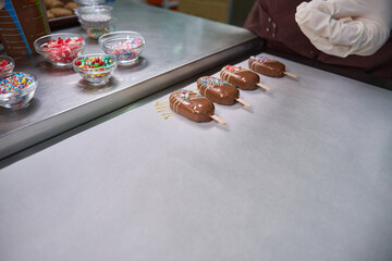 Pastry chef is decorating batch of cakesicles on kitchen countertop