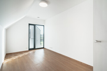 An empty attic room with a wooden floor and a glass window. The room is clean and tidy, and it looks like it could be used for a variety of purposes.
